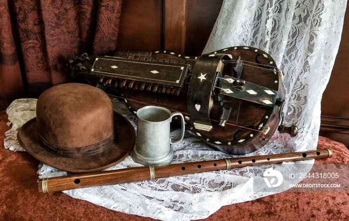 An antique musical instrument called a Hurdy-Gurdy with a bowler hat and tin mug and flute