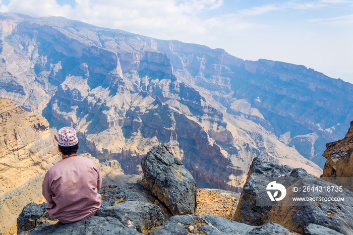 A man is sitting on the edge of  the grand canyon of middle east  at the Jebel Shams mountain in Oman