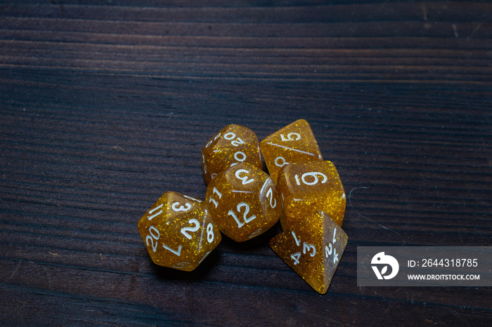 Set of glittery, gold polyhedral game dice grouped together on a wooden table