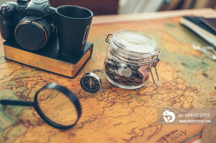 Travel money savings in a glass jar, camera, coffee cup, straw hat and pen on world map. Travel budget concept.