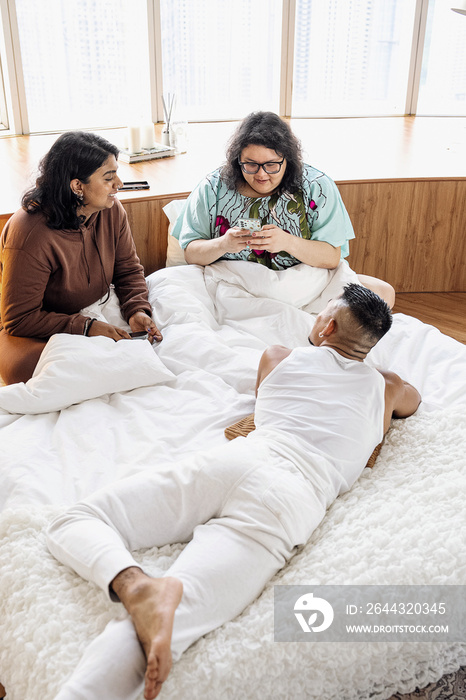 Three friends chatting and laughing together at home in bed