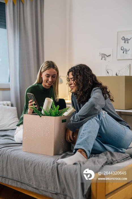 students using mobile phone in dorm room while unpacking