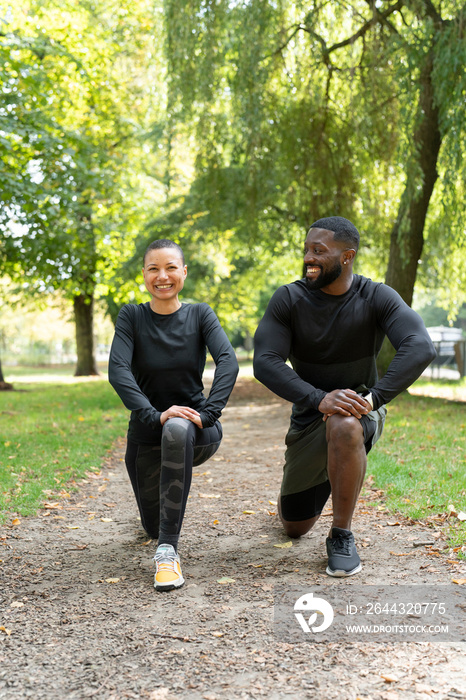 Portrait of smiling man and woman stretching legs in park