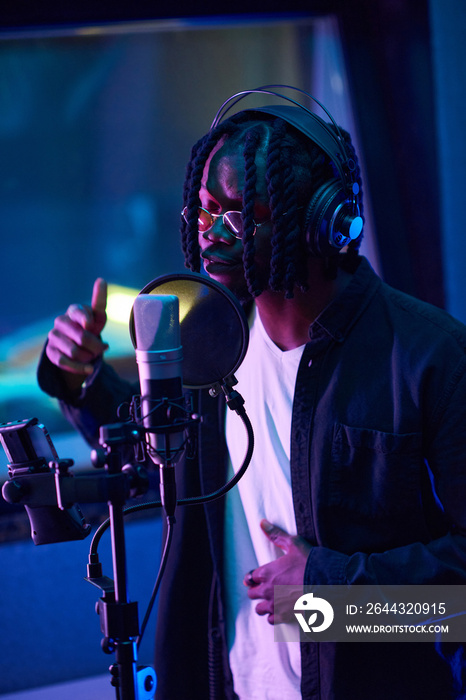 African young singer in headphones singing to microphone, he writing a new song in the recording studio