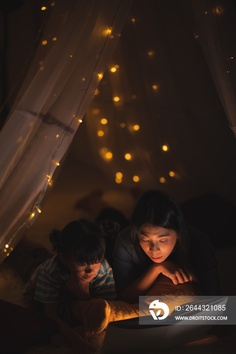 young Asian mother read the story in the book for her daughter children on the bed at home, family and motherhood learning concept