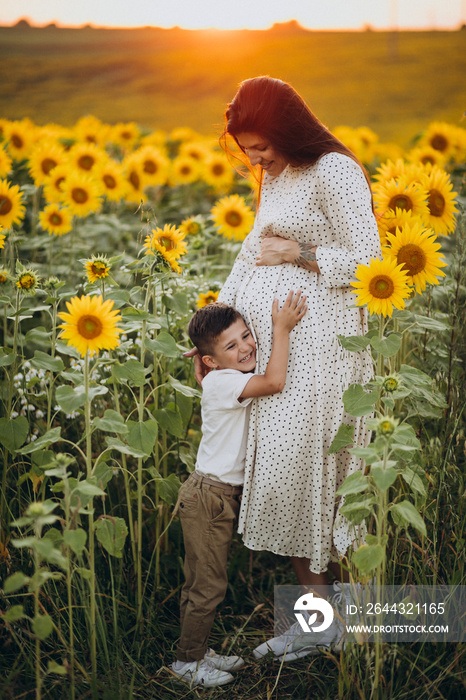 Pregnant youg woman with her son in a sunflower field