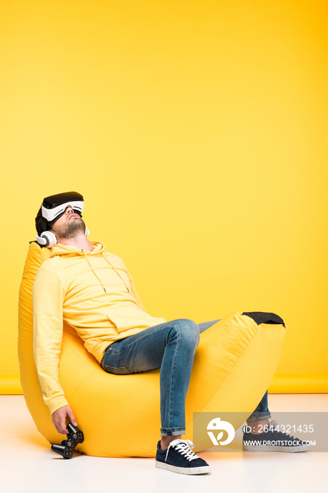 man on bean bag chair with joystick in virtual reality headset on yellow
