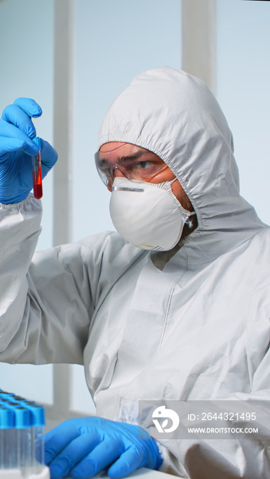 Scientist in sterile chemistry suit analysing blood sample from test tube. Viorolog researcher in professional lab working to discover medical treatment against covid19 virus.