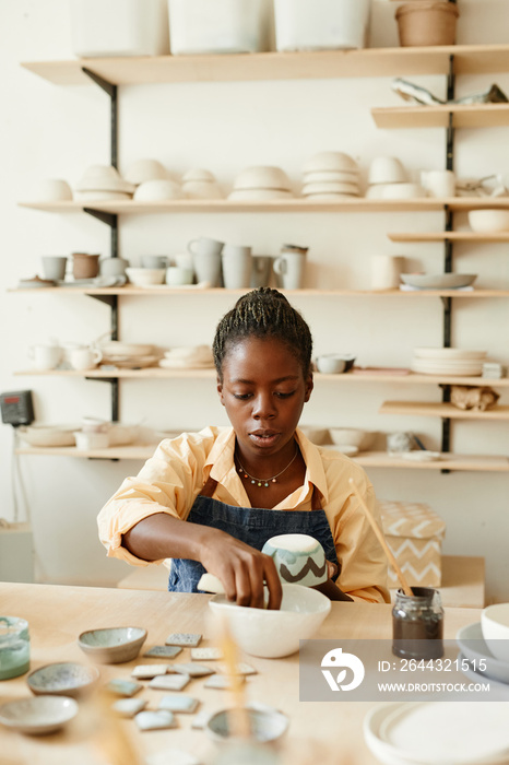 Warm toned portrait of creative African American woman decorating ceramics in pottery workshop, copy space