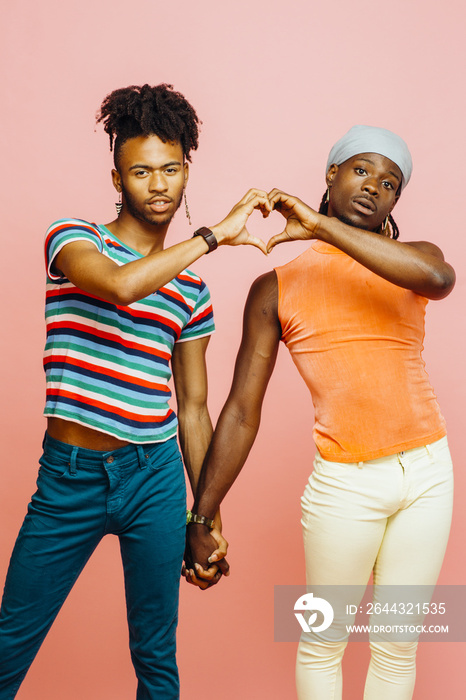 Happy love/ Portrait of two men standing and holding hands while making a heart shape with their hands