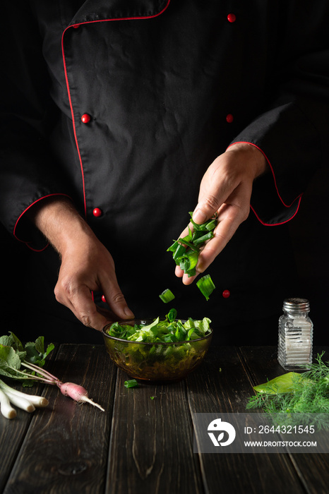 Adding chopped green onions to a fresh vegetable salad by the hands of a chef in the kitchen. Vegetarian dinner