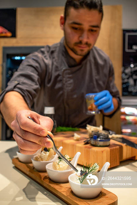 Young chef placing a piece of saffron with tweezers on a plate of appetizers. Amuse bouche. Restaurants and fine dining concept.