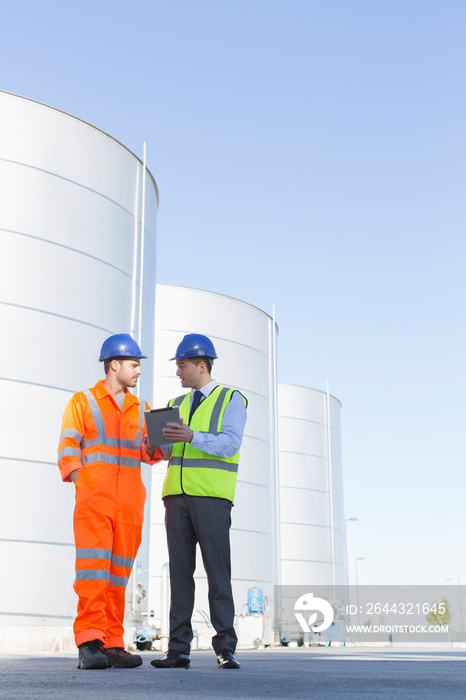 Male worker and manager talking below storage tanks on dairy farm