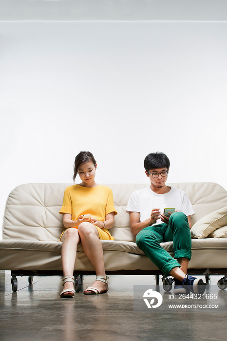 Young adults sitting on sofa using smartphone