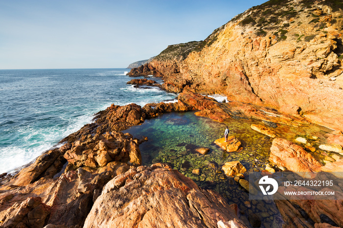 A person stands at the edge of a pristine ocean pool at the base of a cliff on a beautiful coastline on the Great Australian Bight.