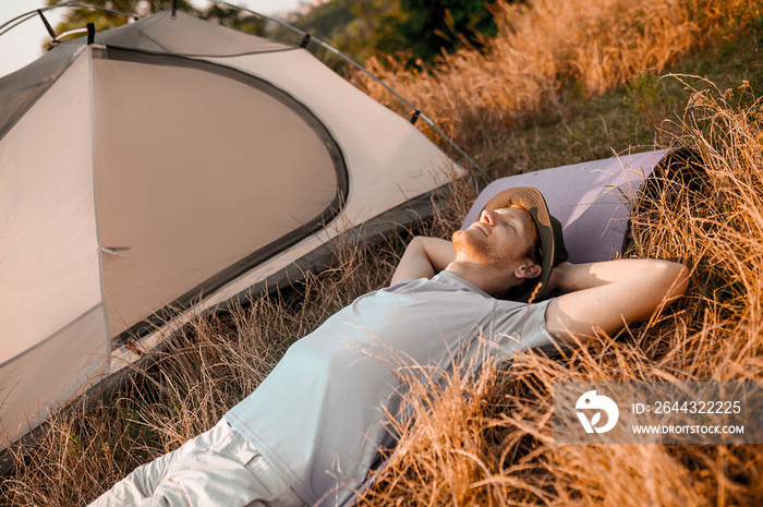 A man laying on the grass near his tent and sleeping