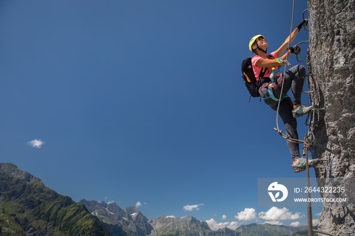 Pretty, female climber on a via ferrata - climbing on a rock in Swiss Alps