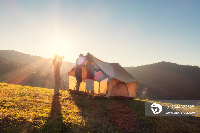 Group of friends pitching a tent on campground hill in the sunset