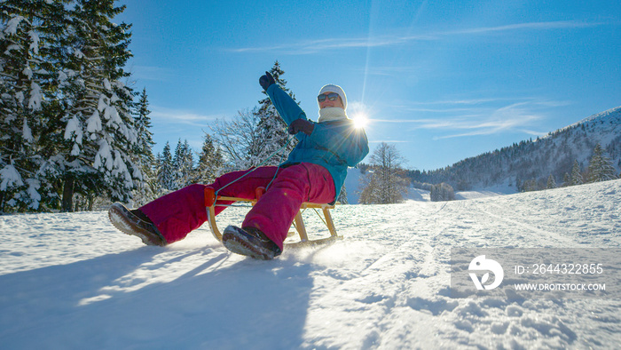 LOW ANGLE Woman outstretches her arm while sledding down snowy hill on sunny day