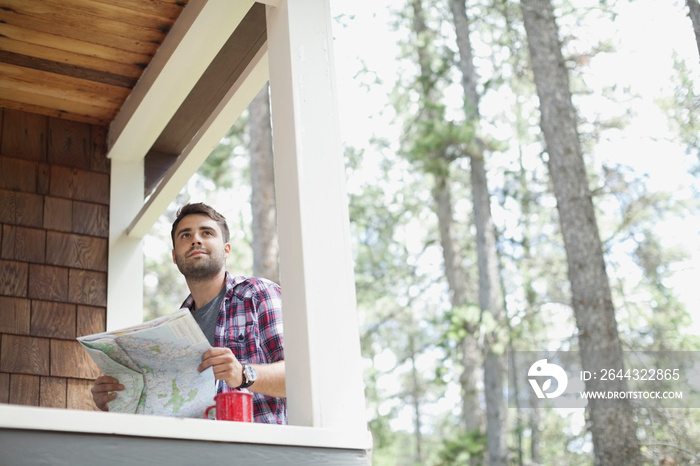 Young man sitting on cabin porch looking at map