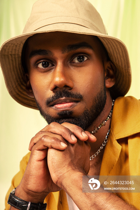 Malaysian Indian man posed in front of a cloth background, styled in a yellow shirt and hat