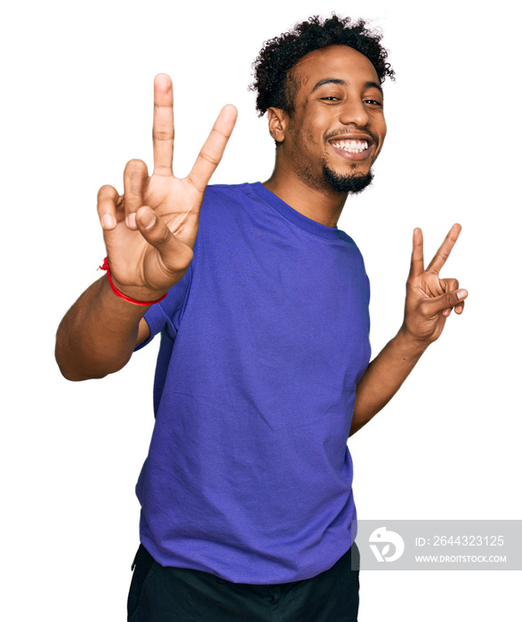 Young african american man with beard wearing casual purple t shirt smiling looking to the camera showing fingers doing victory sign. number two.