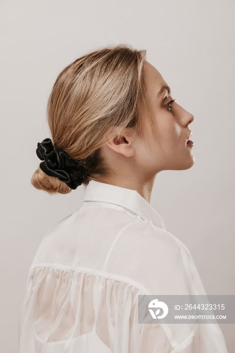 Profile portrait of gorgeous young blonde with classic hairstyle, pure skin and white blouse looking aside isolated over beige background