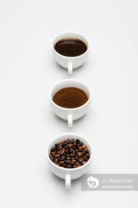 cups with beans, prepared and ground coffee on white