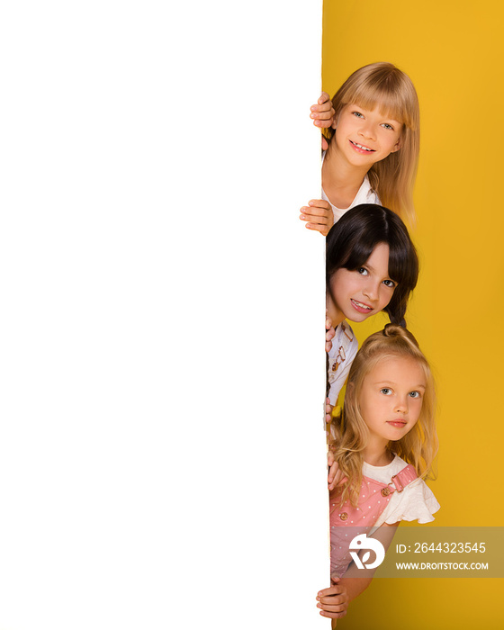 A group of three children of a girl with a white Board on a bright yellow background. Banner, free space for your ads, text. Billboard