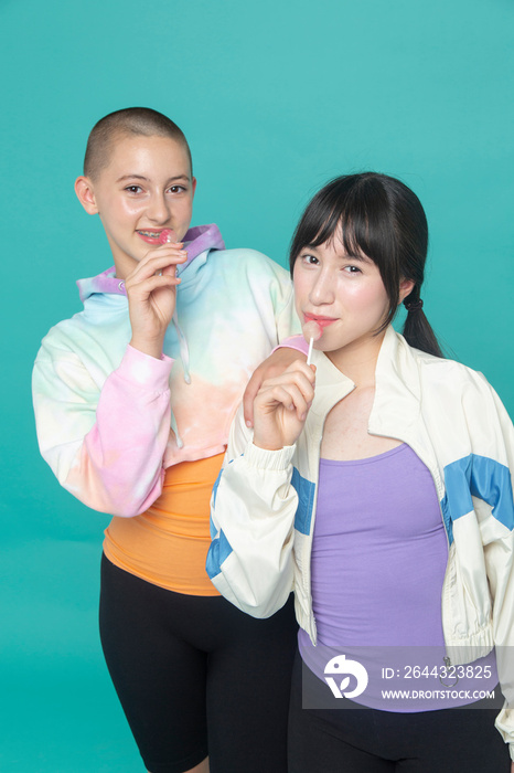 Studio portrait of two smiling girls with lollipops