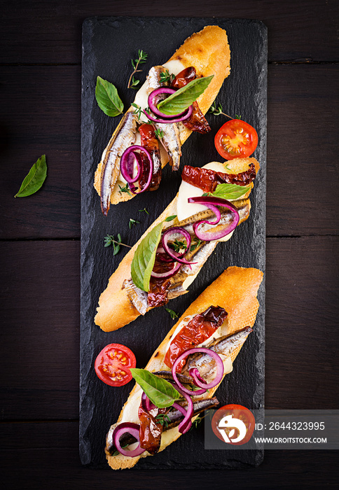 Tapas - Spanish bar food. Bruschetta with slices of sun-dried tomatoes,cheese mozzarella and anchovies on dark background. Top view