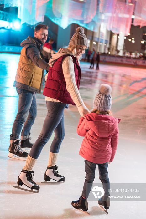 beautiful happy young family holding hands on skating rink