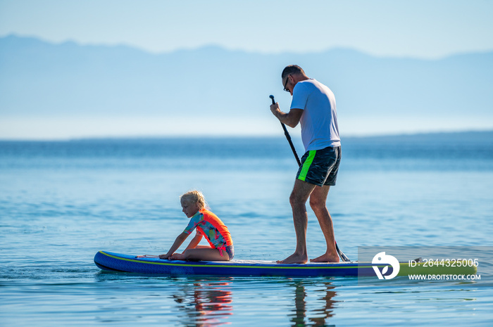 Father and daughter riding SUP stand up paddle on vacation.