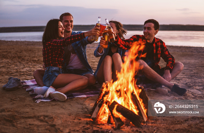 Camp on the beach. Group of young friends having picnic with bonfire. They drink beer