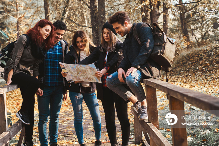 Group of friends have a nice trip at autumn golden leaf park, they are using a map to try to understand where they are.