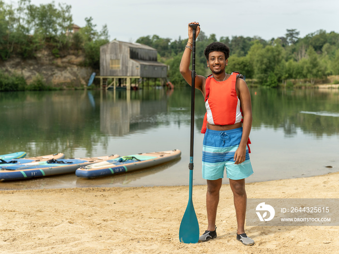 Portrait of young man standing with oar on beach