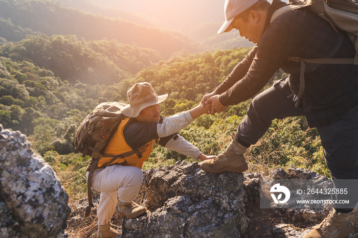 Two Male hikers climbing up mountain cliff and one of them giving helping hand. People helping and, team work concept.