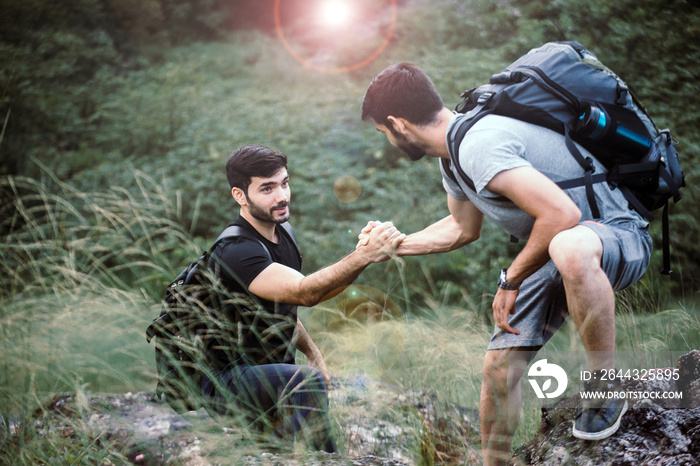 Backpackers man getting help to friends climb a rock,Helping hand,Overcoming obstacle concept