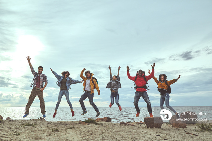 Touching the sky. Full length portrait of joyful friends jumping at the seaside and holding their hands up