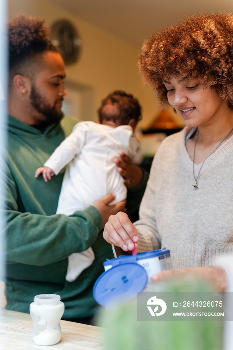 Father holding baby daughter and mother preparing baby food at home