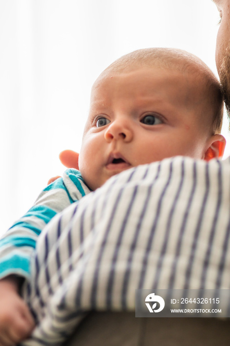 Little baby boy with reflux problem burps and spits in his father’s arms, with cotton cloth on father’s shoulder. Common baby feeding problem.