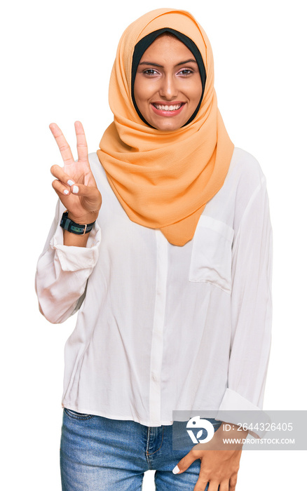 Young brunette woman wearing traditional islamic hijab scarf smiling with happy face winking at the camera doing victory sign. number two.