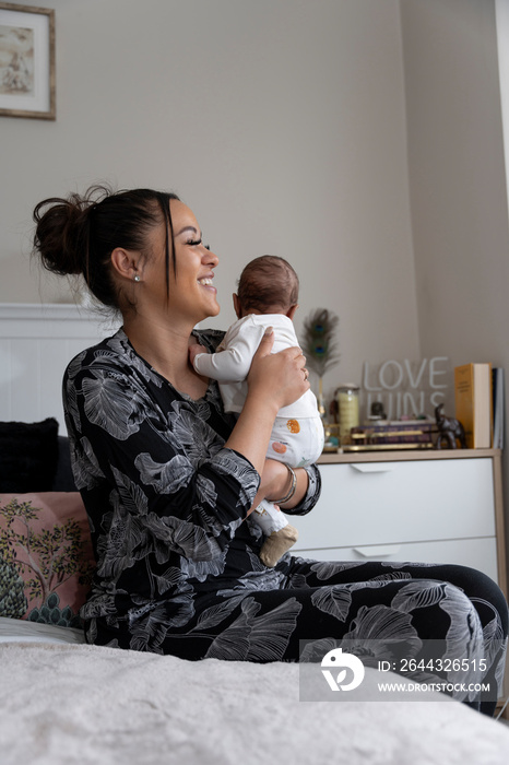 Mother carrying newborn baby girl while sitting on bed at home