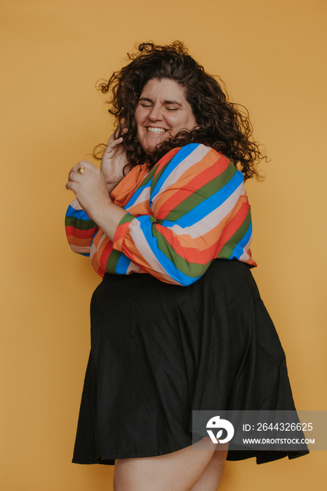 portrait of a plus size woman wearing a rainbow blouse laughing eyes closed