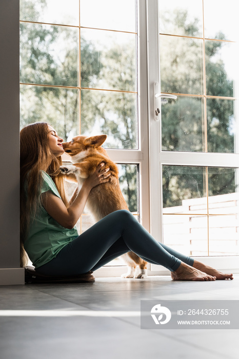 Girl and Corgi dog at home. Young woman sitting and play with Welsh Corgi Pembroke. Lifestyle with domestic pet.