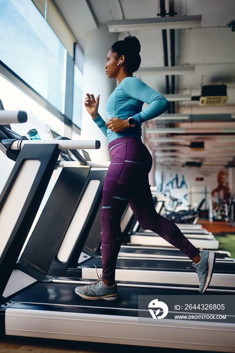 African American athlete jogging on treadmill during her sports training in gym.