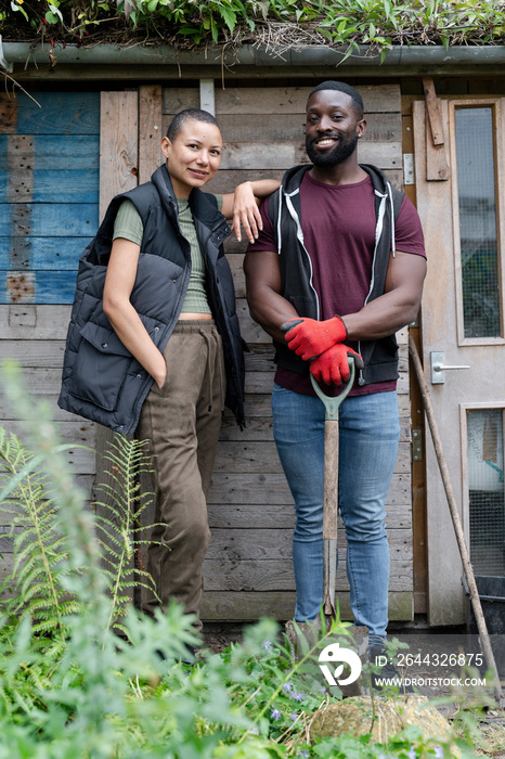 Portrait of smiling couple standing in front of hut in urban garden