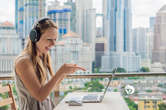 Young woman teaches a foreign language or learns a foreign language on the Internet on her balcony against the backdrop of a big city. Online language school lifestyle