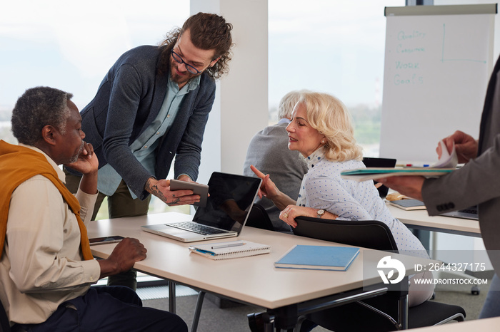 A group of senior students sit in a classroom with their teacher and work on a school project.