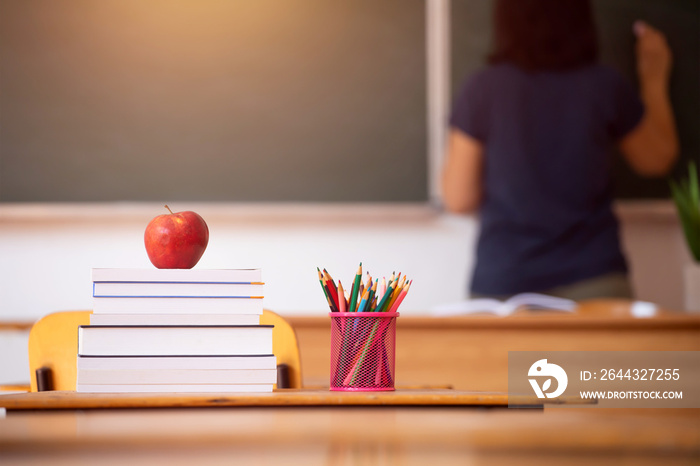 Pencils, apple and books, teacher and blackboard in the background. Education concept.